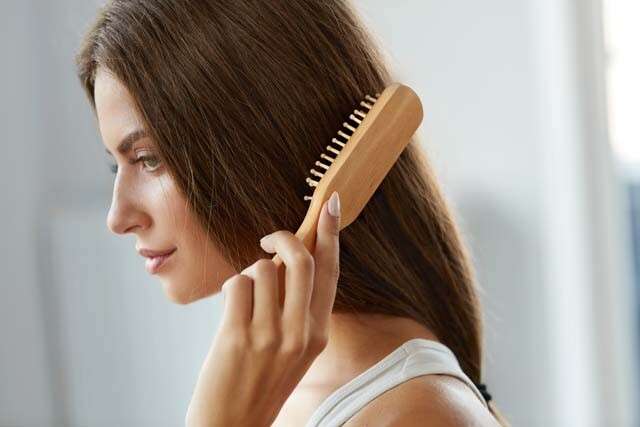 A woman brushing her hair with a wooden comb, showcasing the Science of Sleekness with Ammonium Thioglycolate.