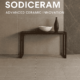 Modern ceramic tile display in a stylish interior featuring Sodiceram products including beige wall tiles, light grey floor tiles, and a dark marble-patterned feature wall, with a minimalist wooden console and decorative objects.
