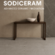 Modern ceramic tile display in a stylish interior featuring Sodiceram products including beige wall tiles, light grey floor tiles, and a dark marble-patterned feature wall, with a minimalist wooden console and decorative objects.